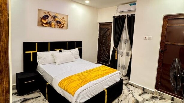 A bedroom with a bed, a nightstand, a wall-mounted artwork, a door with curtains, and a fan.
