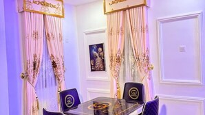 A room with a table and chairs, a framed picture on the wall, and curtains with a gold pattern.
