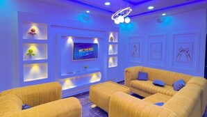 A modern living room with a large flat-screen TV, yellow sofas, and a ceiling light fixture.