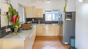 A modern kitchen with a central island, a refrigerator, and a microwave. - Quiet 3-suite house with 4 bedrooms - Assured water - Between sea and mountains. (Baie-Mahault)