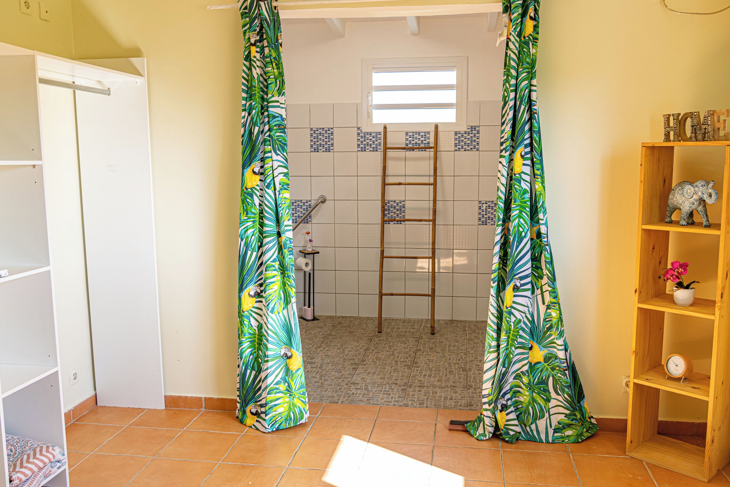 A bathroom with a shower curtain, a wooden ladder, a shelf with decorative items, and a tiled floor.