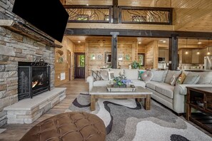 A spacious log cabin interior with a stone fireplace, a large sofa, and a dining area. - Catawba Falls Retreat, Views, Hot Tub & Game Room (Black Mountain)