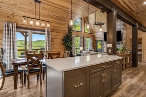 A spacious kitchen with a large island, wooden cabinetry, and a stone fireplace. - Catawba Falls Retreat, Views, Hot Tub & Game Room (Black Mountain)