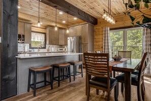 A modern kitchen with wooden cabinets, a central island, bar stools, and a dining table with chairs. - Catawba Falls Retreat, Views, Hot Tub & Game Room (Black Mountain)