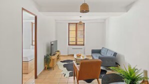 Een moderne woonkamer met een bank, een televisie, een salontafel en een raam met jaloezieën.