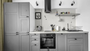A modern kitchen with grey cabinets, a built-in oven, and a coffee maker. There are headphones on the wall and a shelf with kitchen items. - Warsaw Wola Studio – Top Location, Bus&Tram nearby (Warszawa)