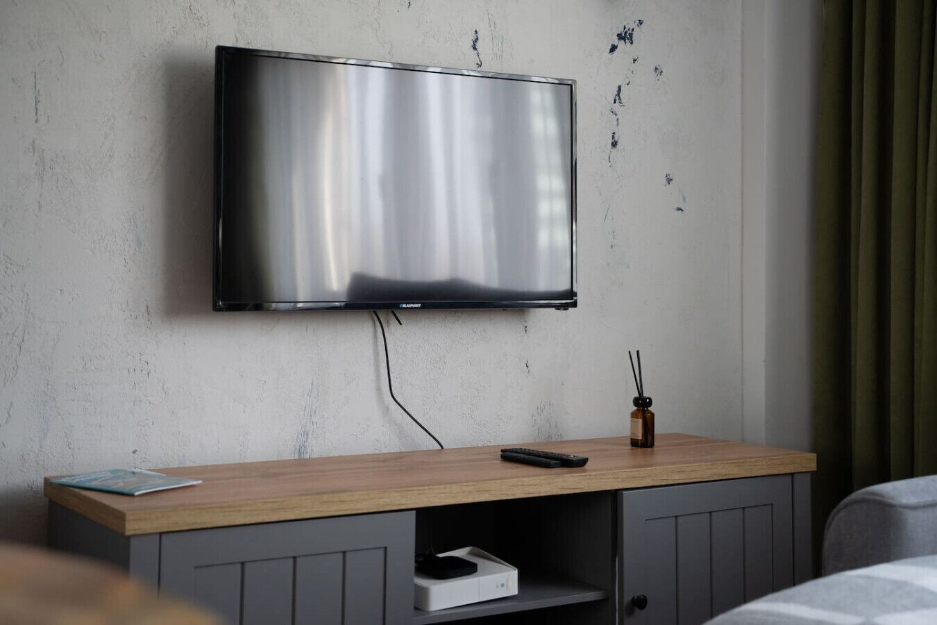 A modern hotel room with a mounted flat-screen TV, wooden console, and a small bottle of perfume.