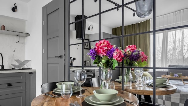 A modern kitchen with grey cabinets, a wooden dining table set with plates, glasses, and cutlery, and a vase with flowers. - Warsaw Wola Studio – Top Location, Bus&Tram nearby (Warszawa)