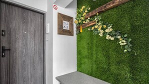 A reception area with a wooden door, a framed sign, a grey reception desk, and a green wall with artificial grass and flowers. - Warsaw Wola Studio – Top Location, Bus&Tram nearby (Warszawa)