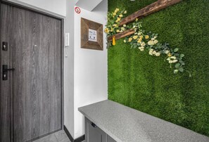 A reception area with a wooden door, a framed sign, a grey reception desk, and a green wall with artificial grass and flowers. - Warsaw Wola Studio – Top Location, Bus&Tram nearby (Warszawa)