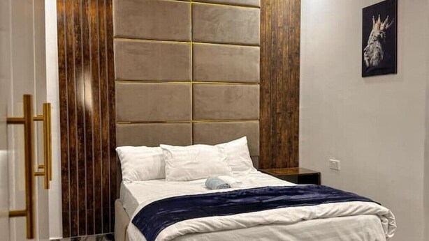 Un dormitorio con una cama grande, cabecera con diseño de panel de madera y una mesita de noche pequeña.