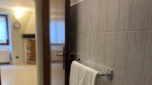 Un baño con baldosas grises, una toalla colgada en un perchero y una puerta que da a otra habitación.