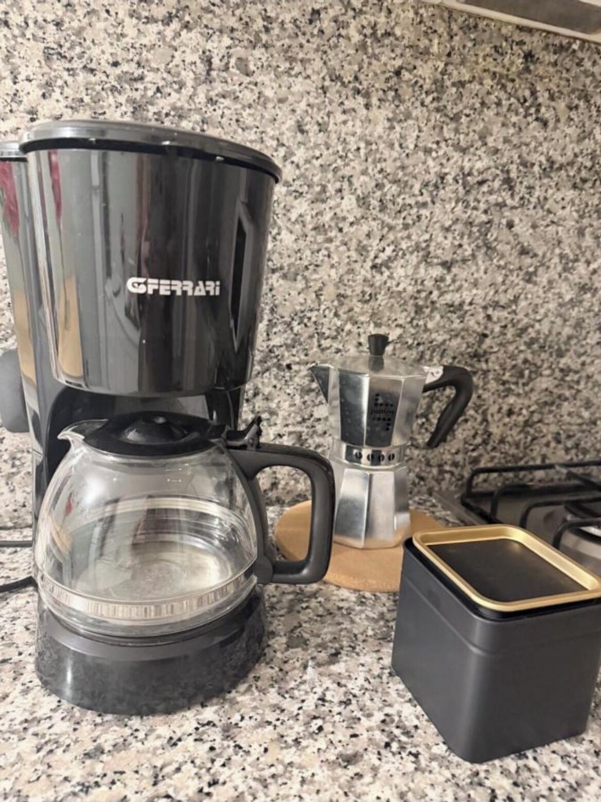 A coffee maker with a clear glass carafe and a black drip tray on a granite countertop.