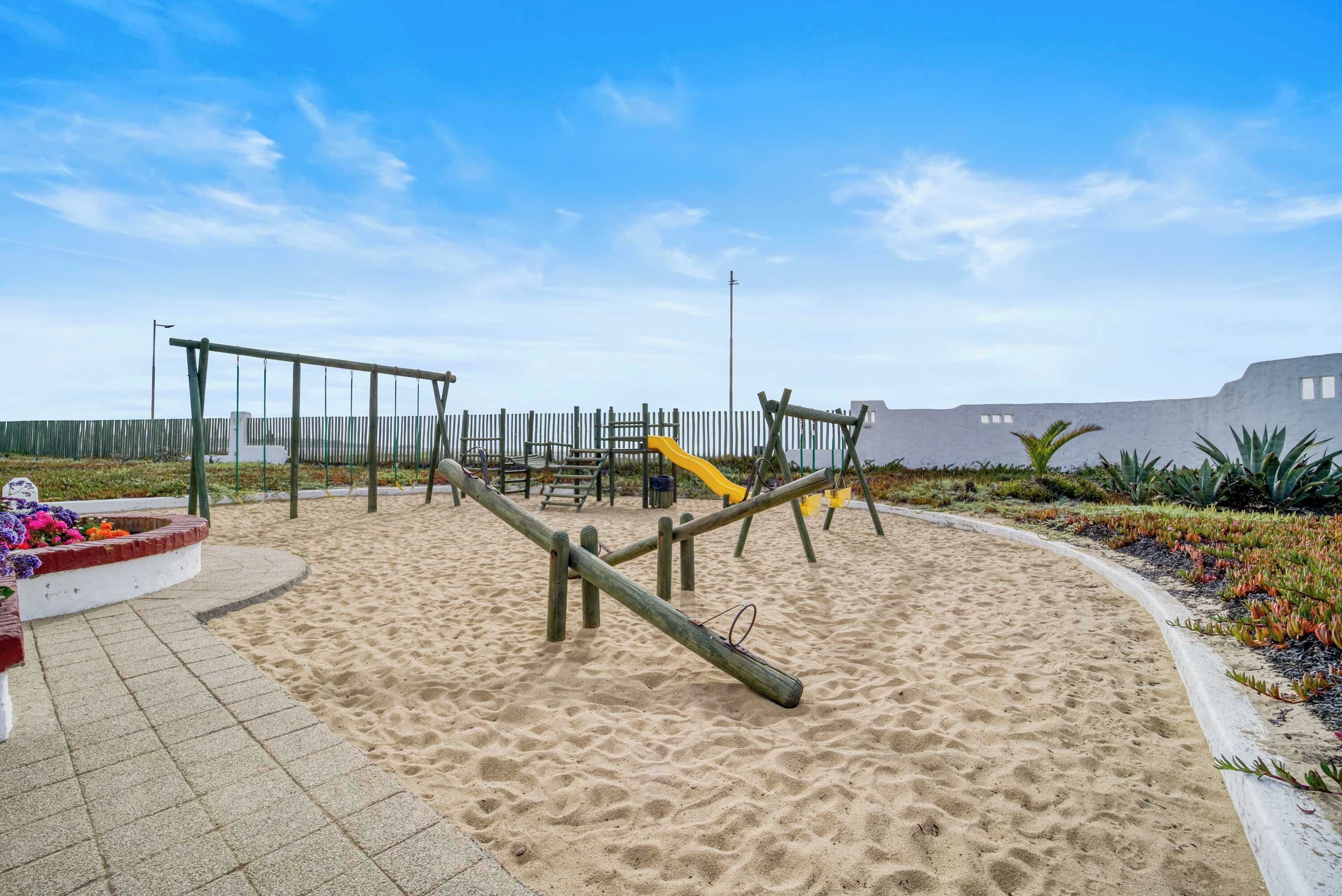 Een speeltuin met zand, schommels en een glijbaan.