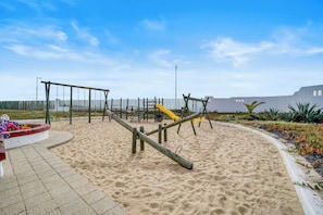 Un parc infantil amb sorra, cadira de balanç i tobogan.