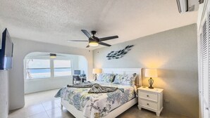 Ein Schlafzimmer mit einem Bett, Nachttischen, einem Deckenventilator und Blick auf den Ozean.