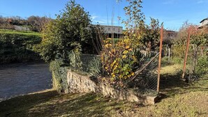 Ein Garten am Flussufer mit einer Steinmauer, einem Metallzaun und einem Gebäude im Hintergrund.