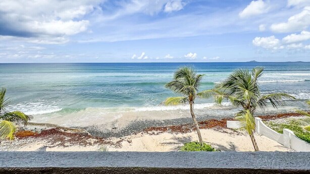 Een strand met helderblauw water, een zandstrand en palmbomen.