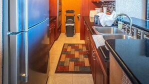 Een compacte keuken met houten kastjes, een roestvrijstalen koelkast, een spoelbak en een vloerkleed met een patroon.