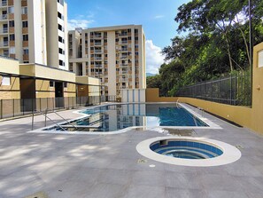 A swimming pool area with a circular hot tub, surrounded by a fence and a building with multiple balconies. - Nativa Park Suites | Exclusive suite with jacuzzi and natural view (Villeta)