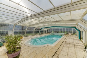 An indoor swimming pool with a glass ceiling, surrounded by a tiled floor, and a potted plant in the foreground. - Country House 'Logis Belledonne - Group' with Mountain View, Shared Pool, and Wi-Fi (Arvillard)