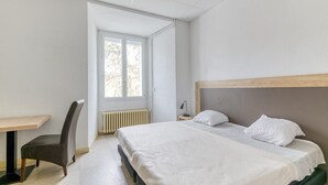 A bedroom with a bed, a chair, a table, and a window.