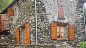 Un bâtiment en pierre avec des volets en bois, un tuyau en métal et un escalier.