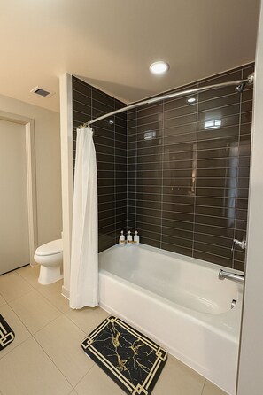A modern bathroom with a bathtub, a toilet, and a shower curtain. - Luxury Downtown Dallas Condo Skyline Views + Parking (Dallas)