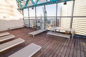 Una terraza en la azotea con piso de madera, sillones blancos y una mesa.