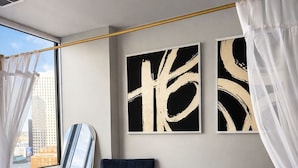 A modern bedroom with a large window, a blue armchair, a small bedside table, and two abstract paintings on the wall.