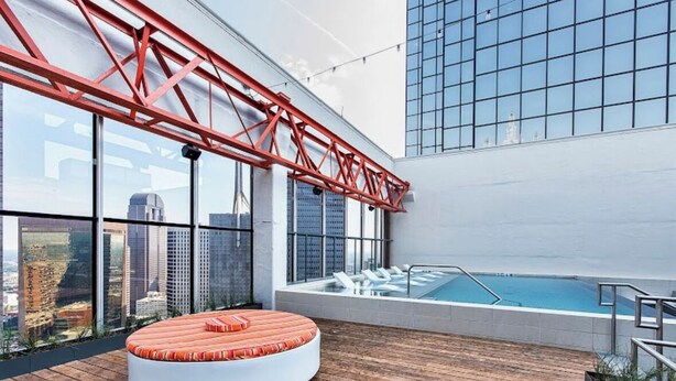 A rooftop pool area with a wooden deck, a circular seating area, and a view of the city skyline.