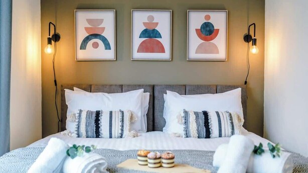 A neatly made bed with white linens, striped pillows, and a small wooden tray with snacks.