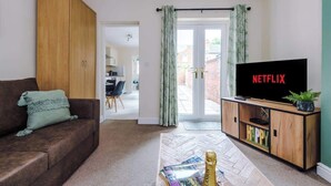A living room with a brown sofa, a wooden cabinet, a television displaying 'NETFLIX', and a door leading to a patio.