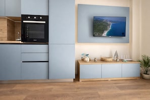 A modern kitchen with a built-in oven, a flat-screen TV mounted above a wooden countertop, and a potted plant on the right. - Tiffany`s Apartment Sea View (Durrës)