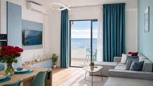 A modern living room with a sofa, a dining table with chairs, a TV, and a view of the sea through a large window. - Tiffany`s Apartment Sea View (Durrës)