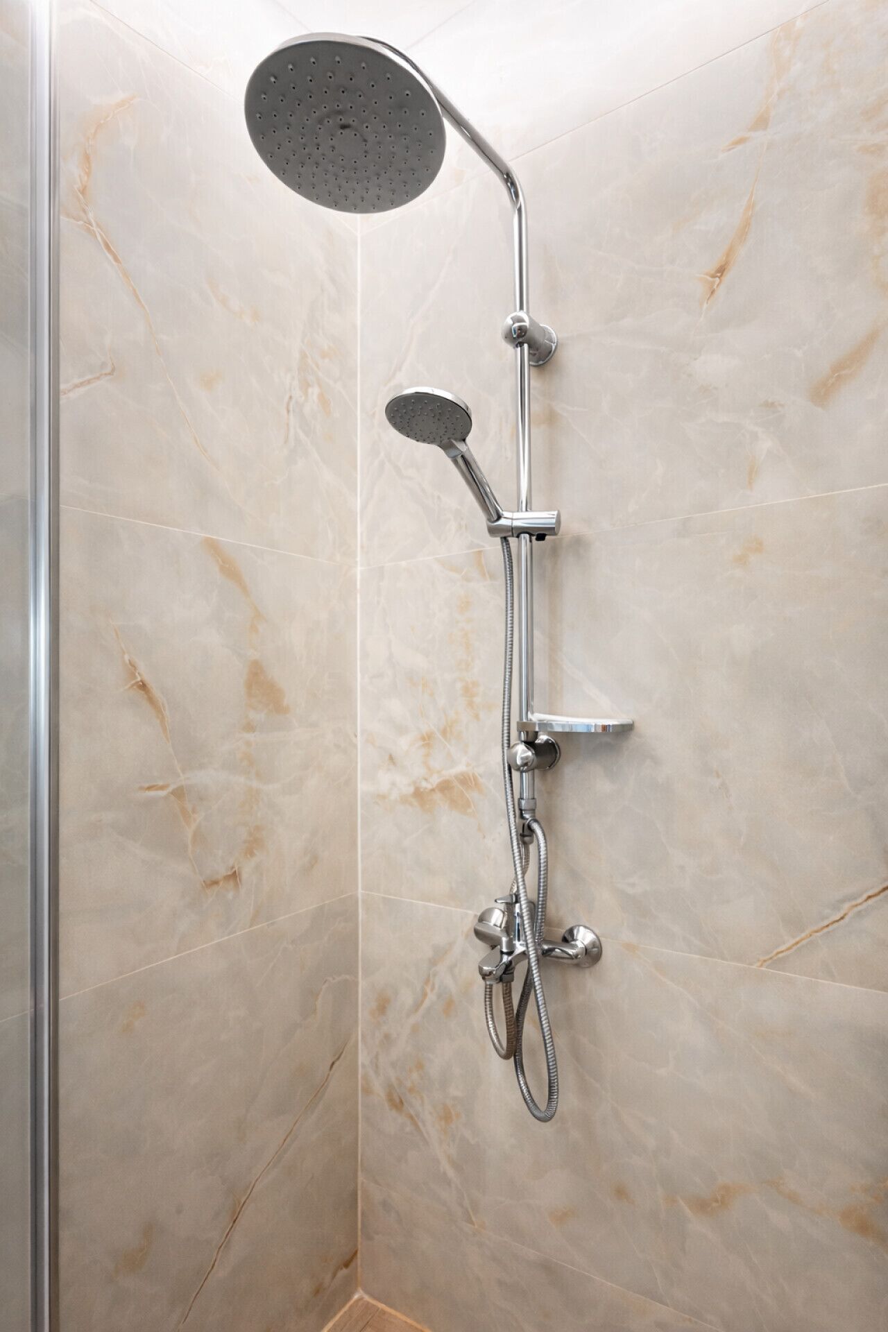 Une douche équipée d’un pommeau de douche à main et d’un pommeau de douche fixe, tous deux fixés sur un mur dont le revêtement imite le marbre.