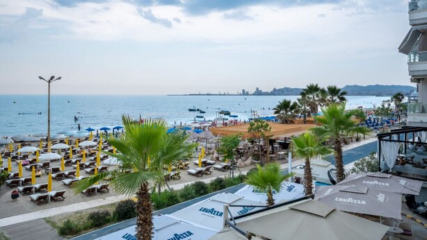 A beachside view with sun loungers, umbrellas, and palm trees. - Tiffany`s Apartment Sea View (Durrës)