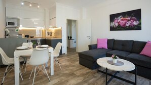 A modern living room with a grey sofa, a dining table with chairs, and a kitchen area with white cabinets and a microwave. - Apartment RELAX Durres (Durrës)