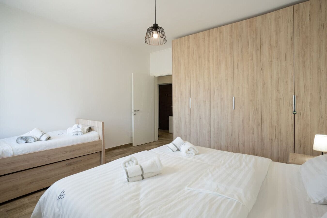 Ein modernes Schlafzimmer mit zwei Einzelbetten, einem großen Kleiderschrank und einer Hängeleuchte.