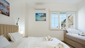 A hotel room with a bed, a wooden dresser, a nightstand, a lamp, and a window with a view of the sea. - Apartment RELAX Durres (Durrës)
