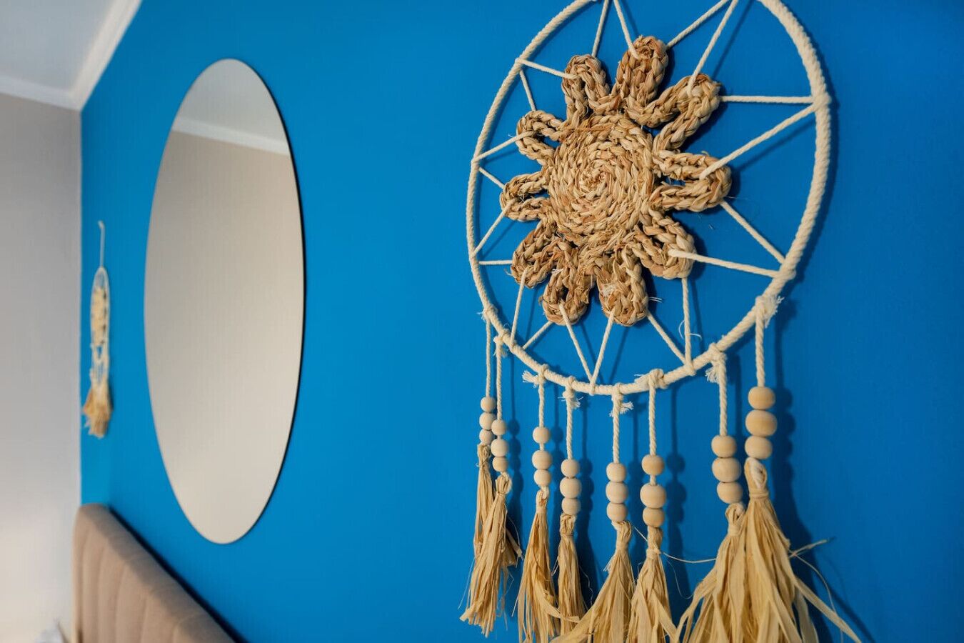 Una pared azul con un espejo redondo y un atrapasueños de macramé con flecos.