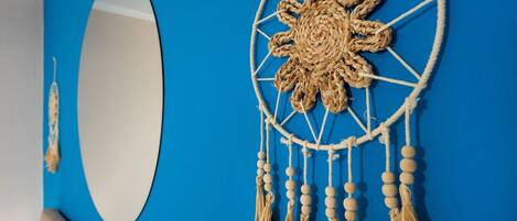 Una pared azul con un espejo redondo y un atrapasueños de macramé con flecos.
