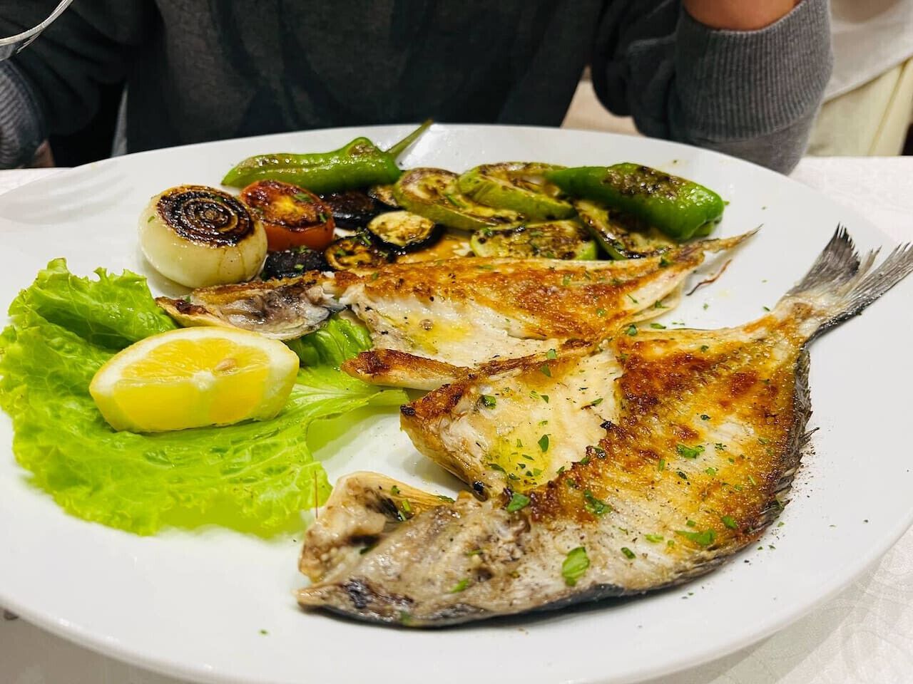 Une assiette contenant du poisson grillé, des légumes et une tranche de citron.