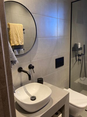 Ein modernes Badezimmer mit rundem Spiegel, Waschbecken in Weiß, Toilette und einer Duschkabine aus Glas.