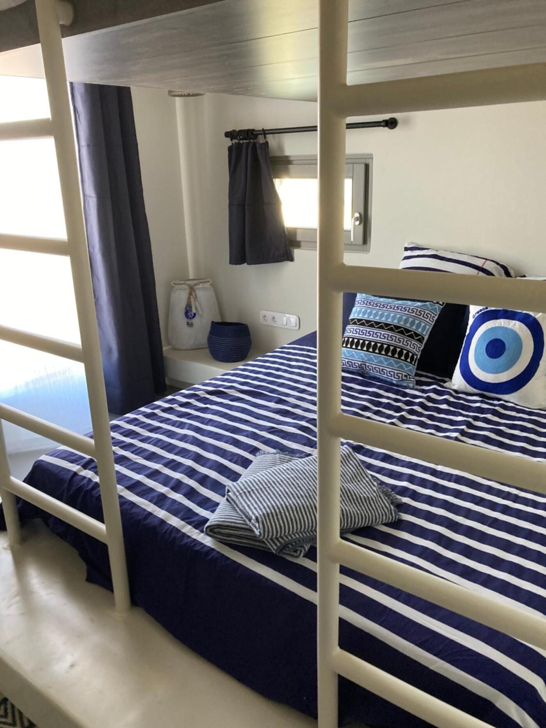 A bunk bed with striped bedding, a small bedside table, a lamp, and a window with curtains.