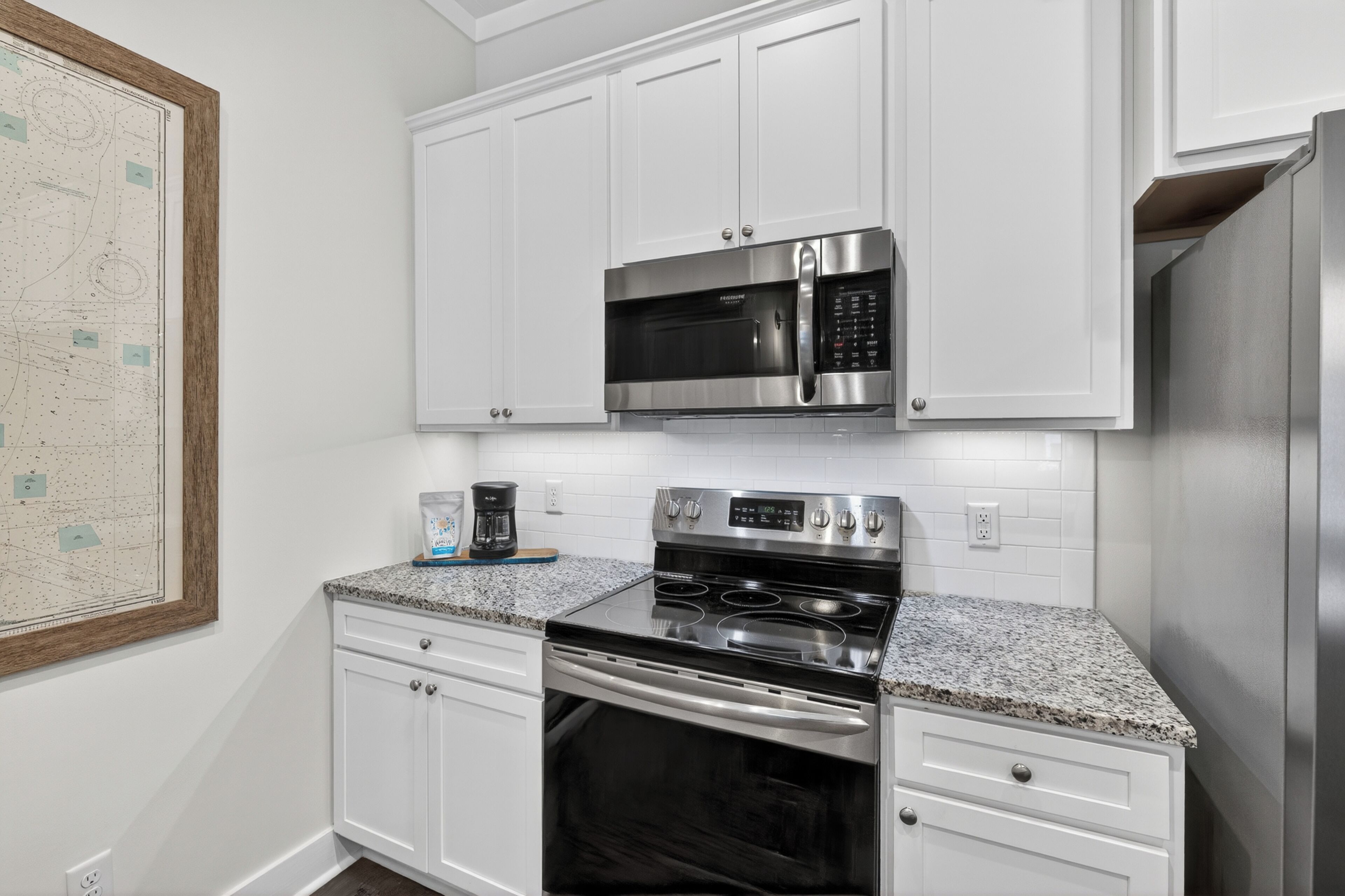 A kitchen with white cabinets, a stainless steel microwave, a stove, and a coffee maker.