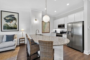 Una cocina moderna con muebles blancos, un refrigerador de acero inoxidable y un comedor con sillas de mimbre.