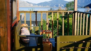Un balcón con vista a un lago y montañas, una mesa con sillas y barandilla de madera.