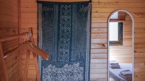 Interior de una cabaña de madera con un tapiz colgante, un espejo y una cama con toallas dobladas.