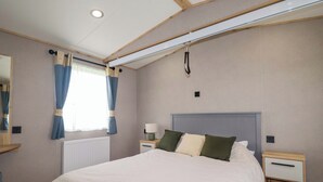 A bedroom with a bed, nightstands, a lamp, a window with curtains, and a ceiling light fixture. - Coastal Escape (Par)